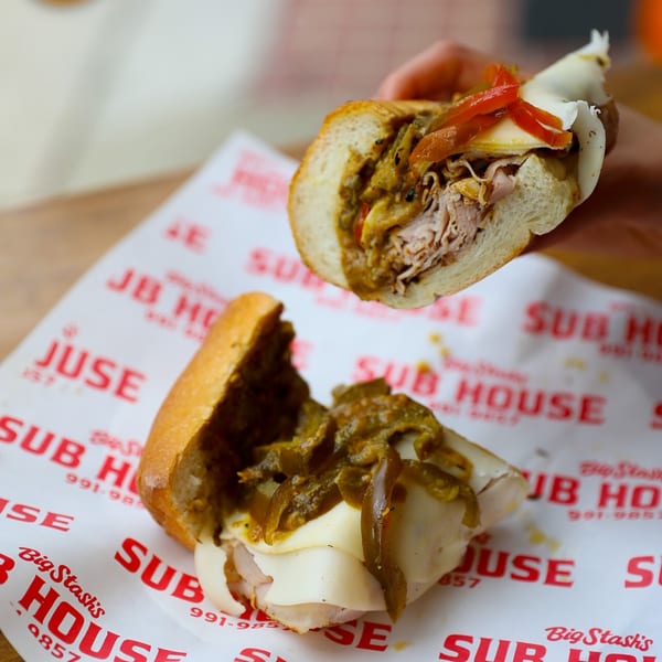 Two halves of a Big Stash's Sub House deli sandwich with meat, cheese, and peppers.