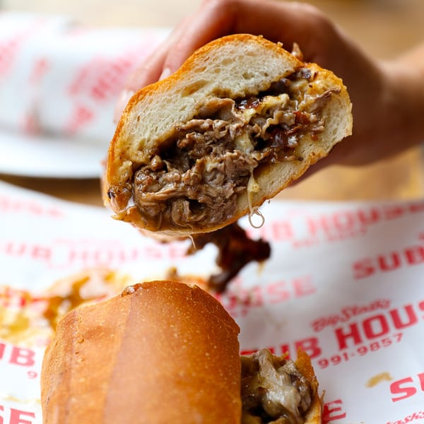 Hand holding a Big Stash's Sub House cheesesteak, with melted cheese and meat dripping.